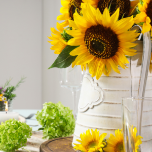 Bride to bee bridal shower table setting with sunflowers in a white metal jug, candle and wine glasses.