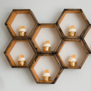 Bride to bee bridal shower cupcakes in gold foil patty cases with white cream swirls and honeycomb wafers on a wooden honeycomb shaped shelf.