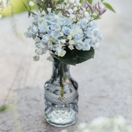 soft blue hydrangea and wildflowers in clear glass decorative bottle vase