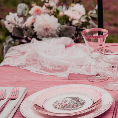 Coquette bridal shower theme inspiration image of vintage table setting with lace, flowers, gold cutlery and gold rimmed wine glasses and plates.