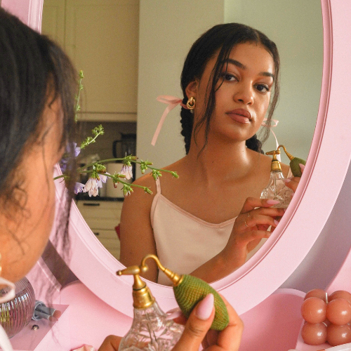 Coquette bridal shower theme inspiration image of vintage mirror and lady with bows in her hair using a vintage perfume bottle.